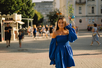 Fototapeta premium Portrait happy young woman wearing blue dress laughing looking at camera standing on street. Urban background