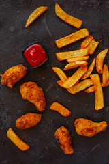 crispy fried chicken and spicy french potatoes with tomato ketchup on a dark Grunge Background