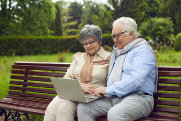 Cheerful senior couple using laptop at park, smiling senior couple using laptop at park, elderly couple looking at their laptop