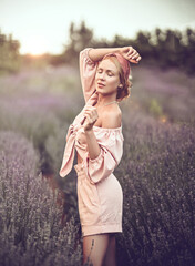 Romantic sexy woman in summer clothes is enjoying a walk through the lavender flower meadow, field. Stands sideways with closed of pleasure eyes, holding hand up, dancing. Summer vibes