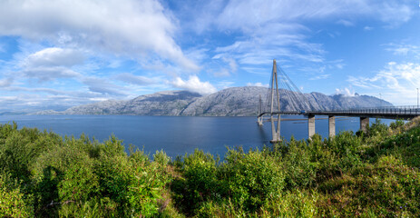 Panoramic view at Helgeland Bridge over blue wide river and Seven Sisters mountain range in summer sunny day under blu sky. Norway