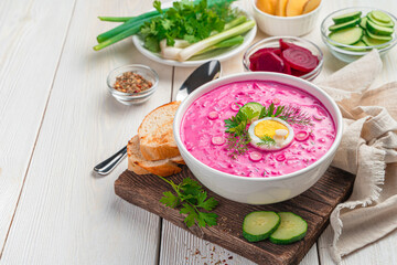 Cold beetroot soup with fresh herbs and egg on a white background. Side view, copy space.