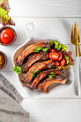  Baked pork ribs with vegetables, mustard and ketchup on white wooden background top view vertical photo