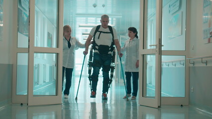 A man in the exosuit is walking with doctors' aid