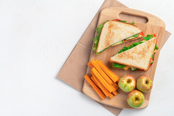 Preparing a school breakfast. Sandwich, carrots and apples on a cutting board on a gray background....