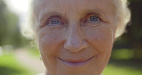 Close up macro bokeh shot of aged woman face looking at camera outdoors