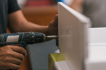 Fototapeta premium Hand of a man using a drill into a piece of furniture in a workshop.