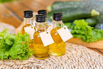 Four types of vegetable oil in small bottles with cardboard labels on the background of salad leaves, zucchini and cucumbers. The concept of healthy healthy food.