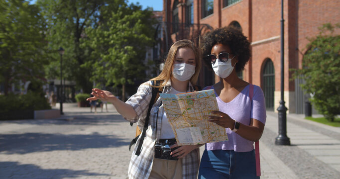 Two female friends in city looking at tourist map and wearing face mask