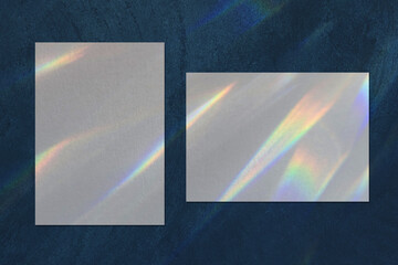 Two empty white vertical and horizontal rectangle a4 poster, business card mockups with overlay of rainbow light refraction caustic effect and shadow on dark blue concrete background