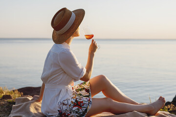 Beautiful lady in straw hat with glass of wine on the beach.