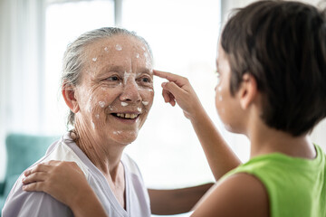 Fototapeta premium Grandmother and little boy putting cream protection on their face