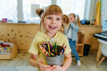 Girl holding color pencils in the kindergarten