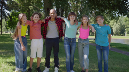 Full length portrait of happy diverse children hug together in park on sunny day