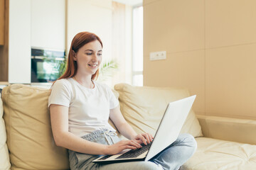 Young beautiful woman freelancer working at home sitting on sofa with laptop online