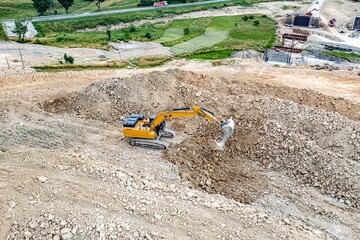 Yellow industrial excavator working on construction site. Drone view.