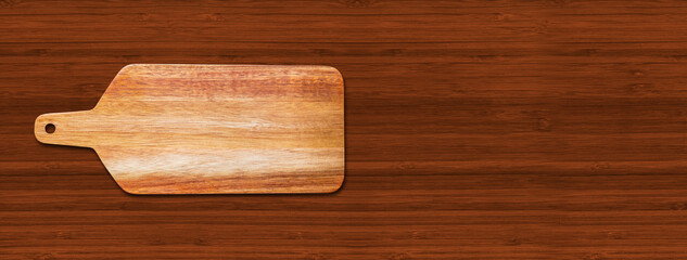 Wooden cutting board isolated on dark wood background. Horizontal banner
