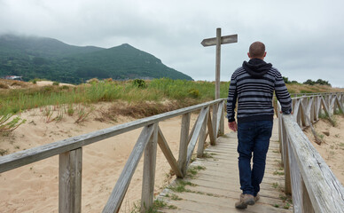 man walking along wooden walkway on cloudy autumn day