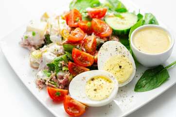 Healthy salad, potato salad with hard boiled egg, shredded ham, cucumber, tomatoes, lettuce and spinach with a honey and mustard dressing pot