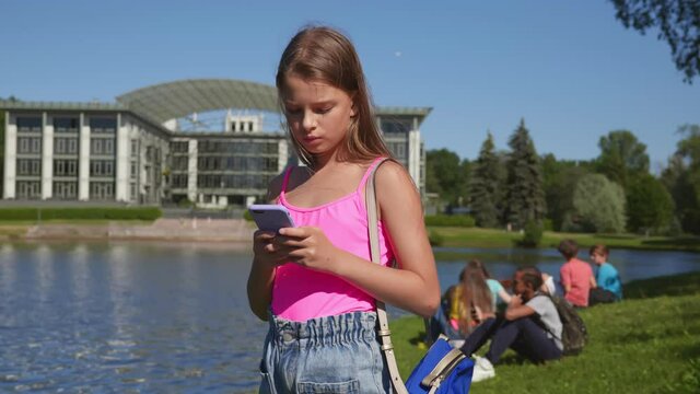 Caucasian pre-teen girl using mobile phone standing in summer park
