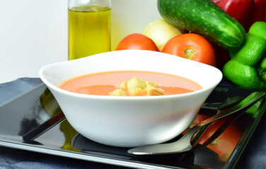 Andalusian homemade gazpacho, from Spain, served on a white plate with breads and exposed with its ingredients. Healthy and beneficial