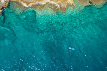 Top view on the man on the stand up paddleboard SUP in the sea with clear turquoise water with rocks at depth