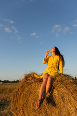 Naklejka na ściany i meble Girl in yellow dress sitting on a haystack on a field.