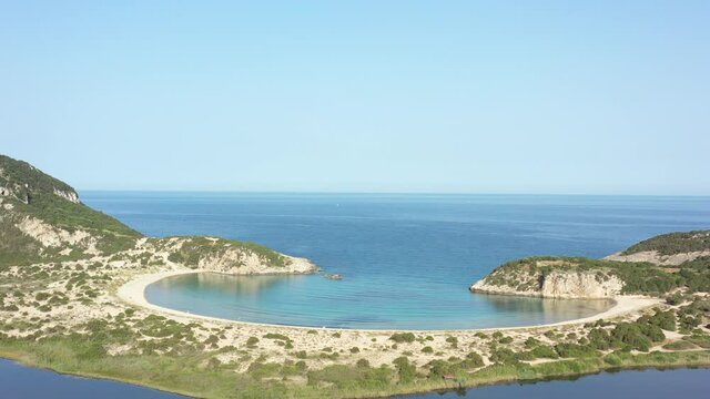 Aerial drone video of semicircular sandy beach and lagoon of Voidokilia, one of the most iconic beaches in Mediterranean sea, with crystal clear turquoise sea, Messinia, Greece