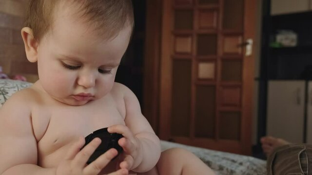 small baby is watching a toy sitting on a couch at home without clothes