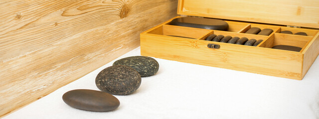 Black massage stones lying near the wooden box with massage rocks on the towel on the table