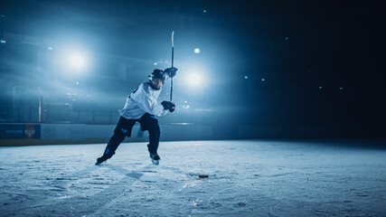 Ice Hockey Rink Arena: Professional Player Shooting, Hitting, Stricking the Puck with Hockey Sticks. Athlete Scoring a Goal. Dramatic Wide Shot, Cinematic Lighting. - obrazy, fototapety, plakaty