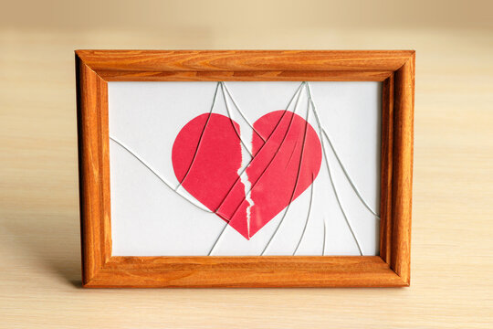 Torn paper heart in photo frame with broken glass