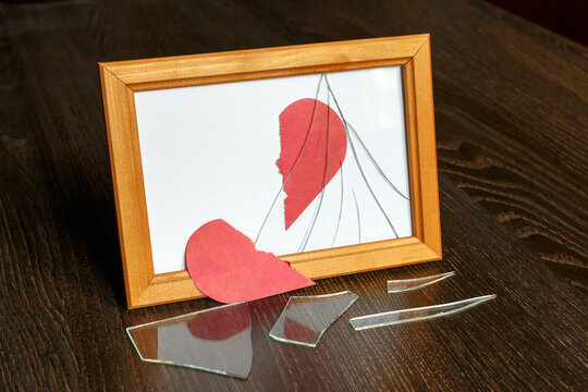 Half of a red paper heart fell on the table next to shards of glass from a damaged photo frame