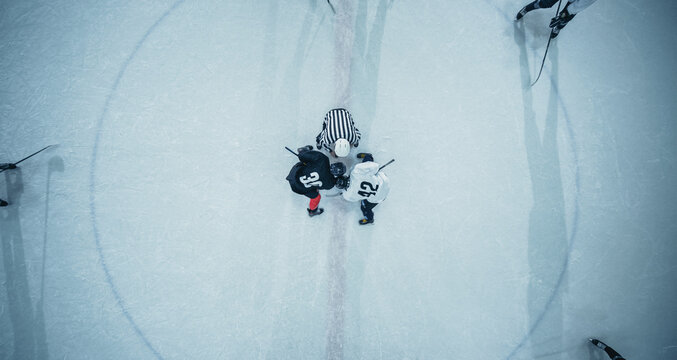 Top View Ice Hockey Rink Arena Game Start: Two Players Face Off, Sticks Ready, Referee Ready To Drop The Puck. Intense Game Wide Of Competition. Aerial Drone Shot