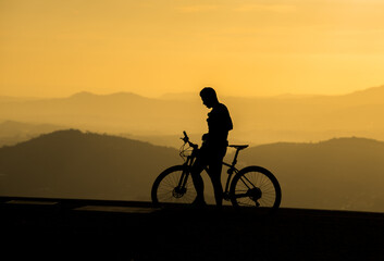 Silhouette of a male cyclist on sunset and mountain layers as background