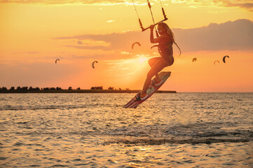 Young woman professional kiter performs a difficult trick in the air on a beautiful background of...