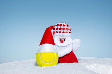 Santa Claus and tennis ball in red santa hat on white snow on winter day. Merry christmas and happy...
