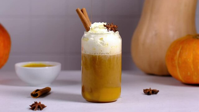 A woman pours caramel syrup over a pumpkin latte and sprinkle with cinnamon.