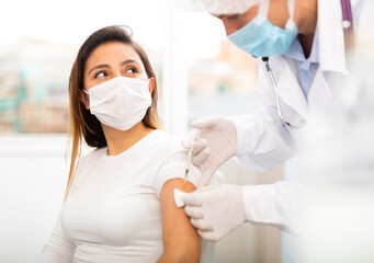 Health care concept, doctor in protective face mask vaccinates woman against coronavirus at...