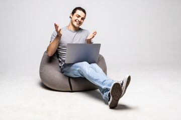Portrait of attractive cheerful guy sitting in chair using laptop calling contact isolated over...