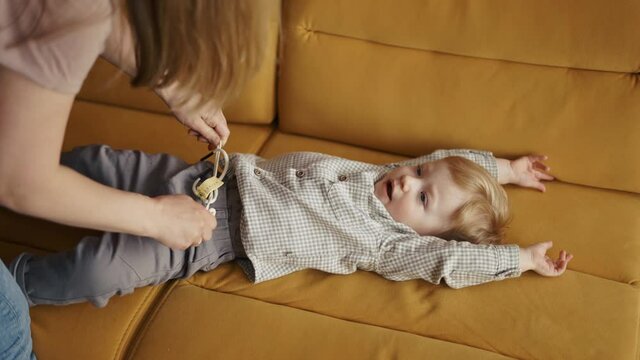 Mom put on pants for her toddler son on sofa