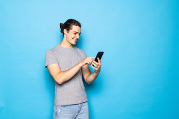 Serious male blogger uses modern smartphone, has attentive gaze at display isolated over blue background. People and modern technology concept