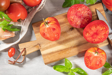 Large variety of tomatoes on rustic kitchen counter. Preparation of tomato sauce with onions and basil