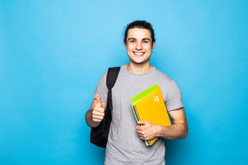 Happy student, holding his backpack and books, standing raising his thumb up, standing on blue...