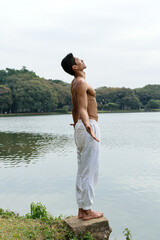 Brazilian young man standing beside a lake with his arms open and looking up.