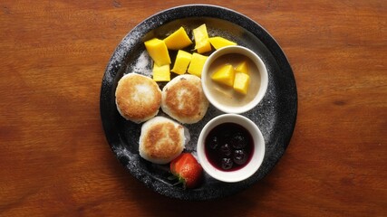 Cream cheese fritter, mango, strawberry, cherry jam, sugar powder on a black plate top shot. Photo a dish of russian syrniki. Delicious breakfast with fried cheesecakes and fruits.Yummy.