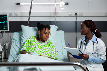 African american doctor and patient talking in hospital ward about diagnosis and treatment for...