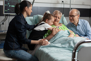 Close-up of granddaughter supporting grandmother hugging her during medicine therapy in hospital ward. Sick retired senior woman resting in bed recovering after medical surgery. Healthcare treatment