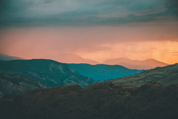 Atmospheric landscape with silhouettes of mountains with trees on background of orange dawn sky. Colorful nature scenery with sunset or sunrise. Sundown paysage in vintage colors and faded tones.