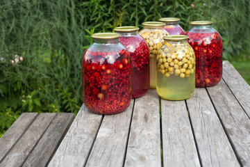 three-liter jars with compote of red currant and orange stand on the street on the table